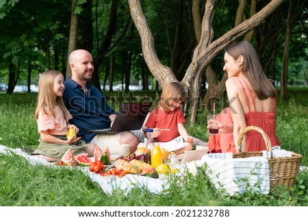 Freelance father does remote work, combining it with family outdoor activities in summer park. Picnic with children. Young family.