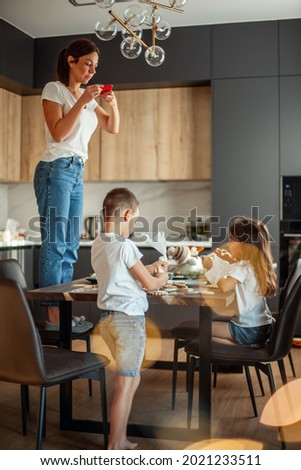 Mom takes pictures of topview as cute daughter and son decorate gingerbread with sugar icing. Stylish home dining and kitchen. Christmas preparation concept.