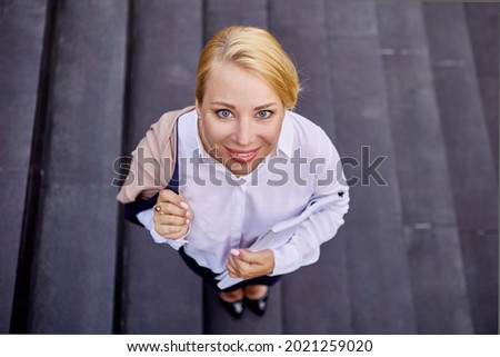Cheerful blond woman is standing on stairs outside.