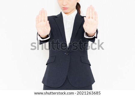 A business woman in a suit standing in front of a white background and making NG gestures