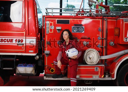 beautiful female doctor in medical coat standing with crossed arms and helmet with fire engine