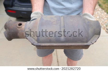 A man holds a large and rusty used catalytic converter that was removed from the vehicle. Converts toxic gases and pollutants from internal combustion engine exhaust. Royalty-Free Stock Photo #2021282720