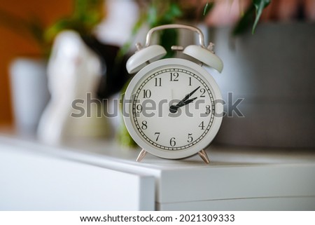 White alarm clock on the shelf with home plants