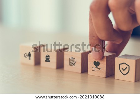 Safety at work concept. Hand holds cubes wooden block with safety icons; safety first, protections, health, regulations and insurance.  Used for banner, beautiful bright background and copy space. Royalty-Free Stock Photo #2021310086