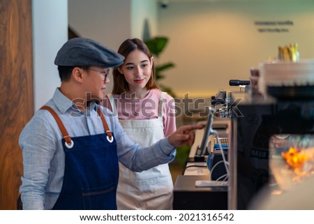 Asian male coffee shop manager teaching young woman staff working on digital tablet. Small business cafe and restaurant owner instruct part time employee preparing service to customers before opening Royalty-Free Stock Photo #2021316542