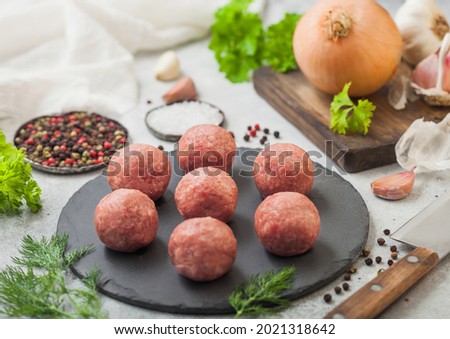 Fresh raw meatballs on stone board with pepper, salt and garlic on light table background with dill,parsley and dill. Top view