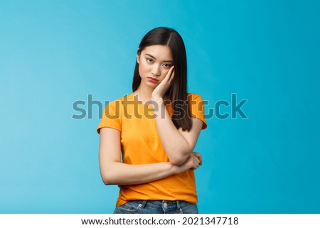 Sad bored asian female student attend boring uninteresting lecture lean face palm, look indifferent express apathy dislike, grimacing and sulking disappointed stand blue background bothered Royalty-Free Stock Photo #2021347718