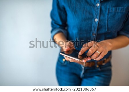 Cropped image of happy girl using smartphone device. Woman in casuals standing in office by a window with phone in hand. Businesswoman with mobile phone in hand.