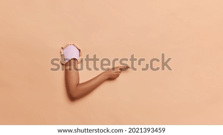 After vaccination. Unrecognizable human breaks through paper background points away into distance with index finger wears adhesive plaster after getting innoculation isolated over beige wall Royalty-Free Stock Photo #2021393459
