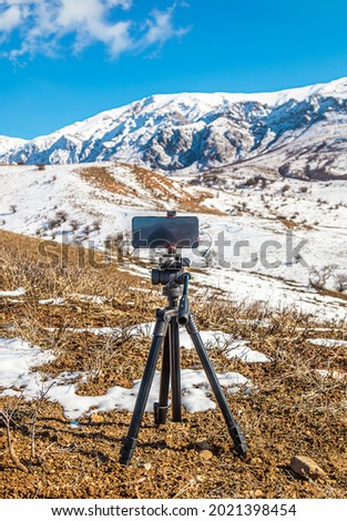 A tripod phone takes pictures of the mountains in the background.