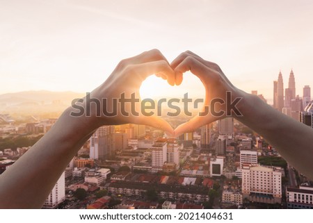 Female hands in the form of heart against sunlight in panorama view of Kuala Lumpur business skyscraper with colorful sunrise morning sky, Malaysia. Hands in shape of love heart, Love concept. Royalty-Free Stock Photo #2021404631