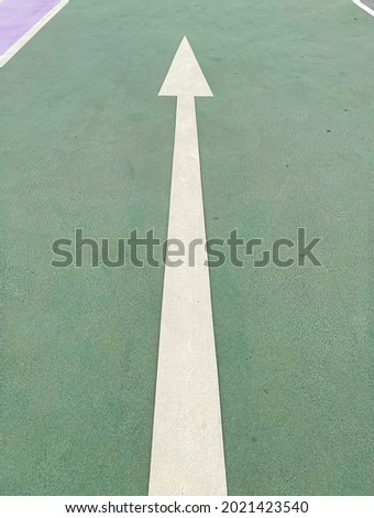 Simple straightforward solution concept: White isolated arrow on green pavement showing direction straight ahead (focus on lower third) Royalty-Free Stock Photo #2021423540