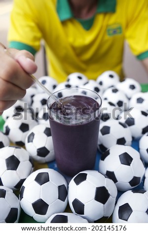 Brazilian soccer player sits eating acai açaí with granola in a glass surrounded by footballs