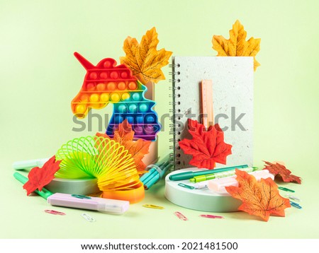 Back to school, office supply concept. Colorful stationery, copybooks set on green background with autumn leaves, geometric podiums, trendy items