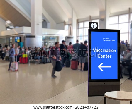 Crowd of people at airport terminal with Corona Virus Vaccination kiosk or info display Covid19 info kiosk, sign, signage or signboard 