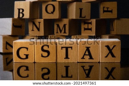 GST and TAX together by letters on wooden beads or block with black background with reflection of letters.