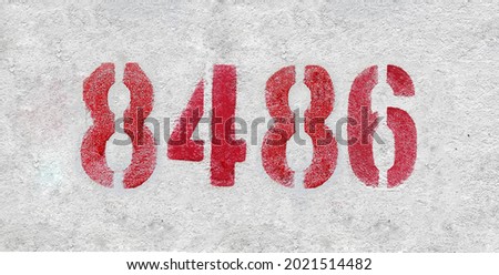 Red Number 8486 on the white wall. Spray paint. Number eight thousand four hundred and eighty six.