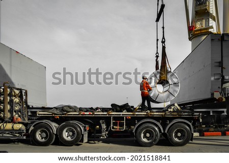 Ship crane put away steel coil on the trailer, work stand on truck placing coil on the support skit. Royalty-Free Stock Photo #2021518841