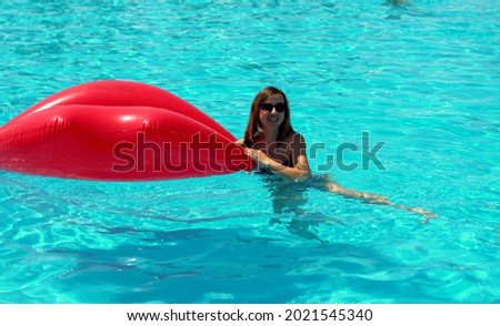 The girl swims in the pool with a mattress in the form of lips