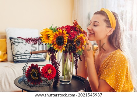 Woman smells bouquet of sunflowers with zinnia flowers arranging in vase at home. Lady enjoys fresh blooms. Interior Royalty-Free Stock Photo #2021545937