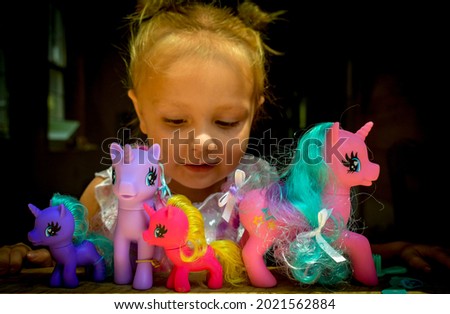 A proud little girl smiling and playing with my little pony unicorn toys she received for a birthday gift- with the sun shinning on her