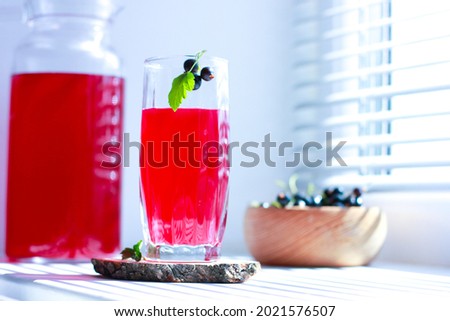 black currant juice with a glass glass on the window in the shade of the blinds, berries, summer soft drinks, healthy food