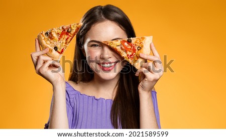 Happy woman holding two slices of pizza near face and smiling, concept of pizzeria advertisement, fast food delivery and eating out, orange background Royalty-Free Stock Photo #2021589599