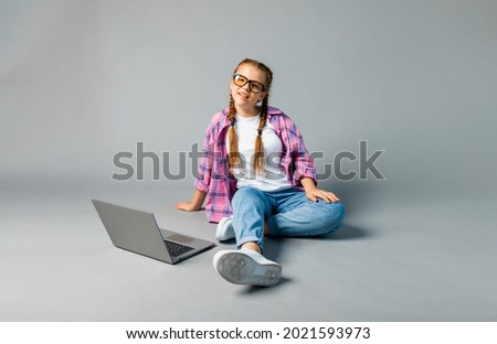 portrait of schoolgirl girl using laptop while sitting cross-legged isolated on gray background