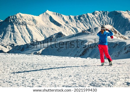 Sporty skier woman taking a picture with phone from the snowy mountains and winter ski resort. Happy skier woman enjoying the view, France, Europe