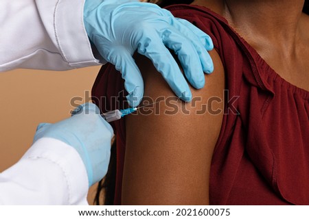 Cropped of nurse hands in protective medical gloves making intramuscular injection in shoulder for unrecognizable black woman, closeup photo. Vaccination, immunization while COVID-19 pandemic