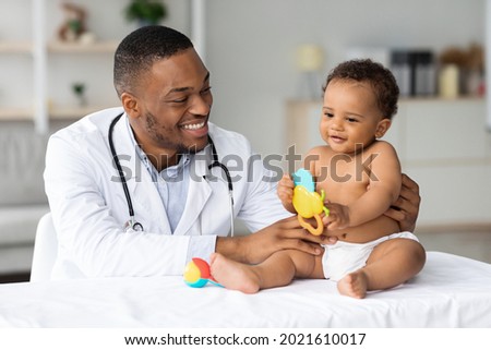 Portrait Of Smiling Black Doctor Making Medical Check Up For Little Baby Patient In Clinic, Handsome Young African American Pediatrist Looking At Adorable Infant Child In Diaper, Closeup Shot Royalty-Free Stock Photo #2021610017