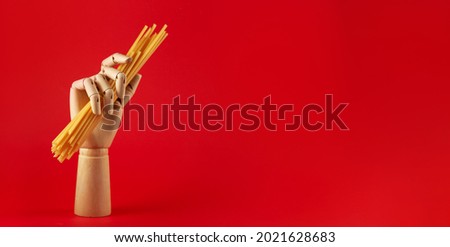 Horizontal banner with wooden hand and dry pasta on red background with copy space. Spaghetti creative concept. Italian food on minimalistic picture