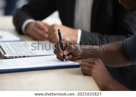 Close up of African American man sign paperwork close business deal with partner or client at meeting office. Biracial ethnic male employee or worker put signature on document make legal agreement.