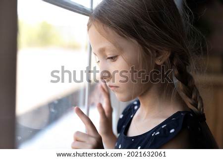 Sad thoughtful orphan child got trauma, feeling depressed, lonely, upset. Serious bored girl standing by window, thinking, touching glass. Childhood problems, abuse, violence in family concept Royalty-Free Stock Photo #2021632061