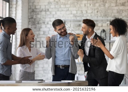 Smiling multiracial businesspeople congratulate colleague with job success or achievement. Happy supportive diverse multiethnic employees greet excited male worker with work promotion. Royalty-Free Stock Photo #2021632196