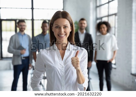 Portrait of smiling young Caucasian businesswoman stand forefront show thumb up give recommendation. Happy female employee or client recommend good quality company service. Review concept. Royalty-Free Stock Photo #2021632220