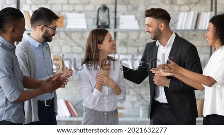 Smiling supportive diverse businesspeople congratulate excited young Caucasian female employee with job promotion or success. Happy multiethnic colleagues greeting woman worker with work achievement. Royalty-Free Stock Photo #2021632277