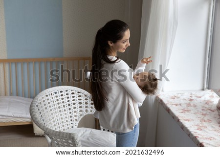 Smiling loving young Caucasian mother lull put to bed little newborn baby daughter in children bedroom. Happy caring mom caress hug breastfeed with small infant kid child. Motherhood concept.
