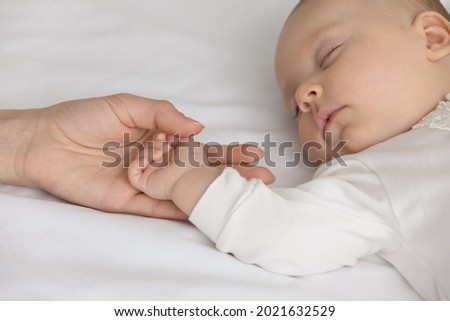 Crop close up of loving mom hold little newborn son or daughter hand sleep daydream in bedroom at home. Caring mother caress lull small baby infant child nap in bed. Motherhood, parenthood concept. Royalty-Free Stock Photo #2021632529