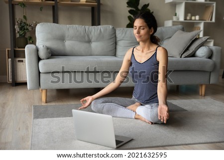 Relaxed woman meditating, practicing yoga online at home, using laptop, sitting on floor in easy seat, breathing fresh air, stress relief, mindful young female involved in internet lesson, webinar Royalty-Free Stock Photo #2021632595