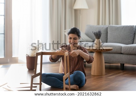 Happy millennial Indian female renter or tenant sit on floor in new house gather shelf. Smiling young ethnic woman put together make build piece of furniture settle in own home. Rental concept. Royalty-Free Stock Photo #2021632862