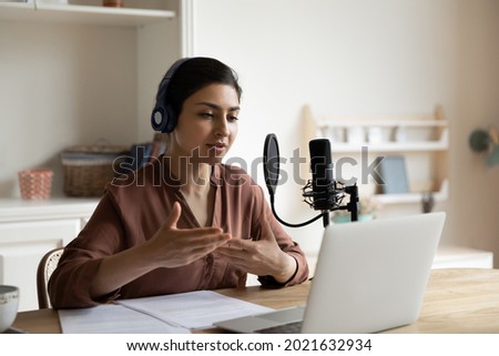 Young Indian female coach or trainer use headphones microphone record live podcast vlog talk on video call on computer. Ethnic female have webcam digital virtual event on laptop. Technology concept. Royalty-Free Stock Photo #2021632934