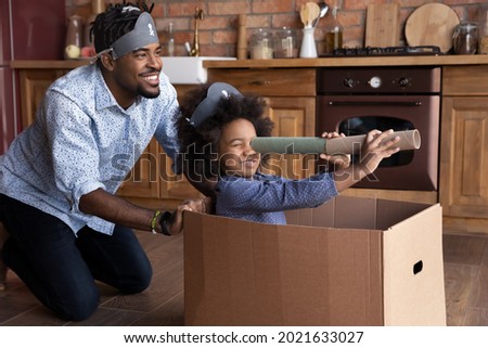 Smiling loving young African American father and small biracial daughter have fun play pirates sail in ship look in spyglass. Happy caring ethnic dad engaged in playful activity with teen girl child.