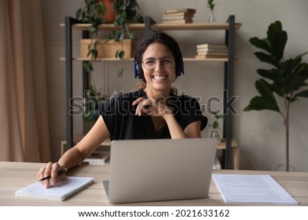 Head shot portrait of smiling woman in headphones using laptop, looking at camera, businesswoman consulting client, involved in internet meeting, excited student studying online, watching webinar
