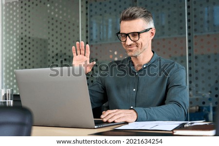 Happy mature business man executive waving hand using laptop computer having video conference call virtual meeting, professional training negotiation remote working online in office. Videoconference Royalty-Free Stock Photo #2021634254