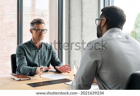 Two diverse business executive partners negotiating at board meeting, manager adviser consulting client discussing financial partnership contract sitting at table in office. Job interview concept. Royalty-Free Stock Photo #2021639234
