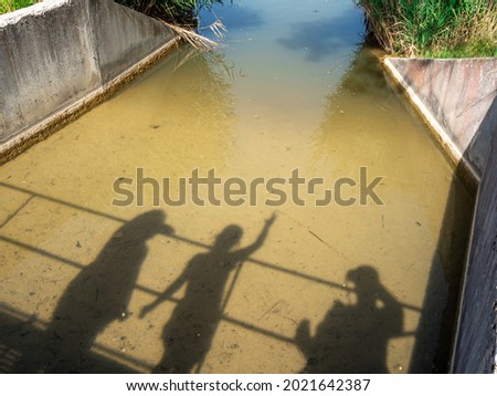 3 people's shadow reflection on little river in summer 