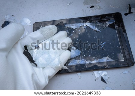 A hand in a white glove holds the broken glass from an electronic tablet, repair and replacement of glasses in smartphones