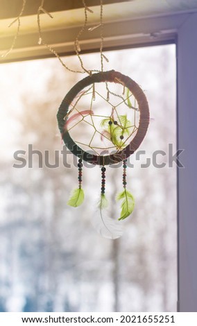 Handmade dream catcher on window background in winter day. Tribal decorative design element. Decor made of the colorful beads and feathers
