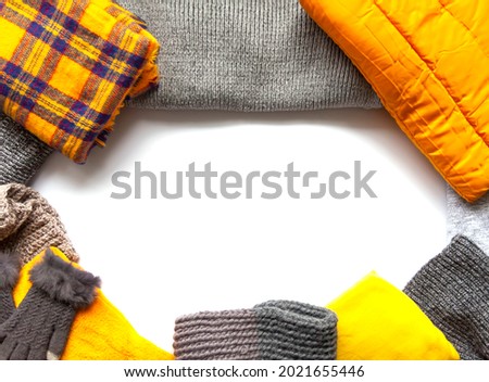 Warm winter wear on white background. Copy space. Yellow and grey trendy fashion colors. Knitted jumpers, jackets, mittens and plaids